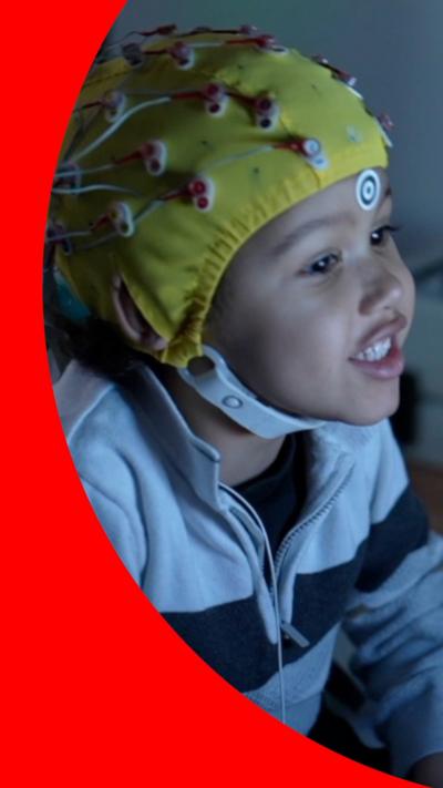 A young child is wearing a yellow, monitoring skull cap with wires.