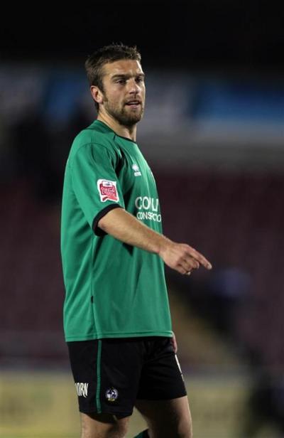 Ricky Lambert in a green football top and black shorts on a football pitch. He is pointing to the floor.