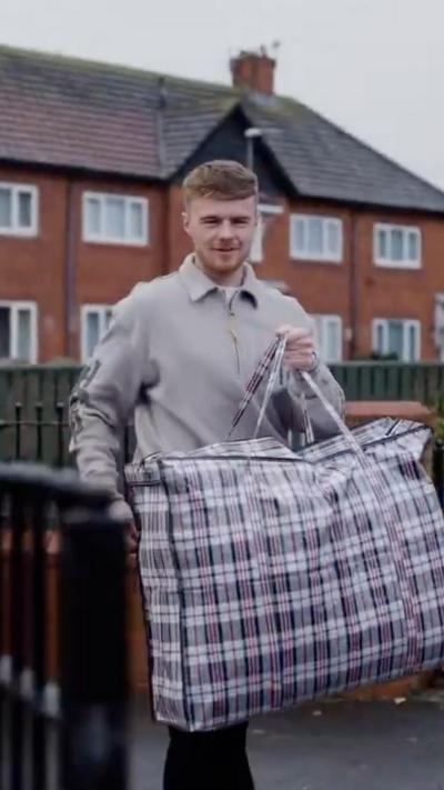 Middlesbrough footballer Tommy Conway carrying a check bag infront of a row of terraced houses