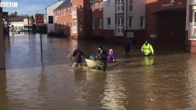 A care worker is helped through flood water