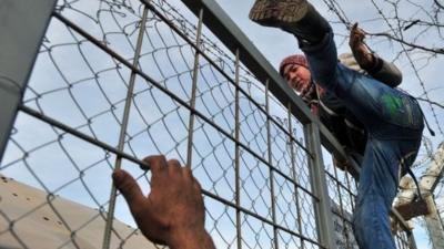 A man climbs over a fence of the Greek-Macedonian border near the village of Idomeni, northern Greece