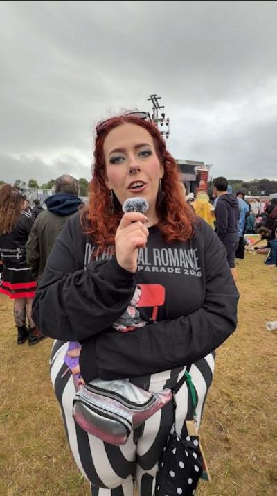 Woman in dark top with shoulder length dark red hair outdoors at a concert.