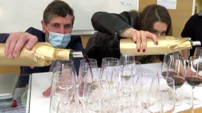 A man and a woman pour two bottles of wine into glasses - one bottle has been into space