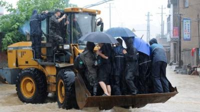 July 11, 2015 shows villagers making their way through flood water on an excavator brought by typhoon Chan-hom in Shaoxing, east China's Zhejiang province