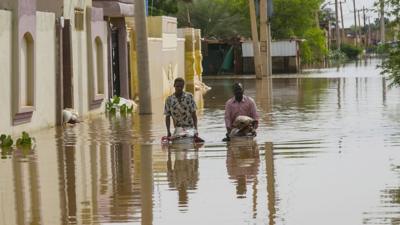 Two men wade through the floodwaters at Umm Dawm district in Khartoum, Sudan