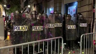 Riot police stand in formation after being pelted with paint