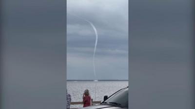 Waterspout stretches from lake to sky as people watch