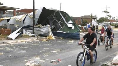 Residents from Sydney"s southern suburb of Kurnell cycle past the damaged homes