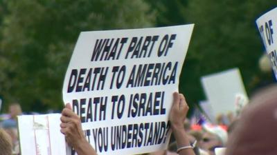 A protester holding a sign reading 'What part of death to America, death to Israel don't you understand?'