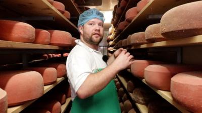 Doddington Cheesemaker flanked by shelves stacked with 10kg wheels of cheese