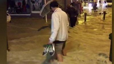 Man holding shoes wading through water
