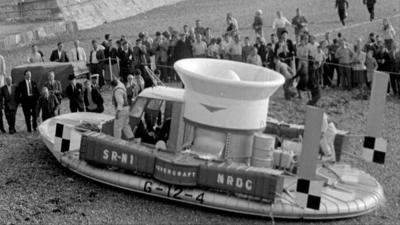 Hovercraft parked on a beach, with a crowd of people standing around it