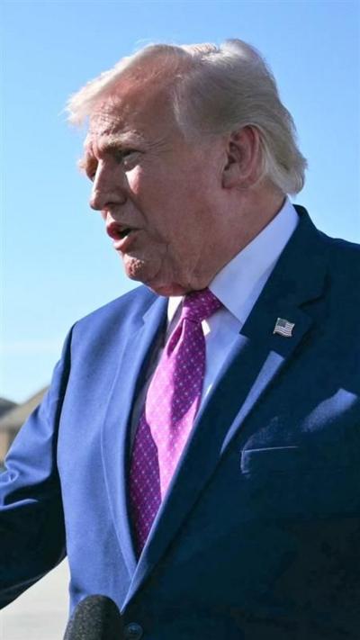 Donald Trump, wearing a blue blazer and pink tie, addresses reporters outdoors. A blue sky is the background.