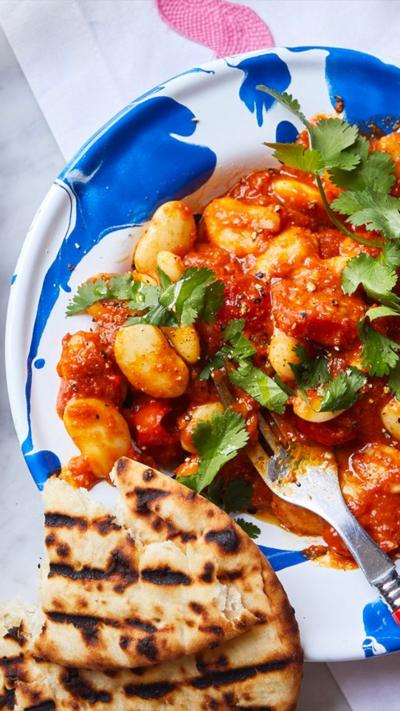 Top down view of a blue and white plate with curried butter beans on a a garnish on top. A and some flatbread sit at the side