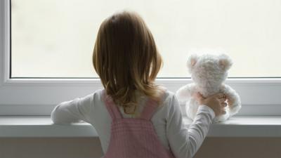 Young girl looking out of the window holding a teddy bear