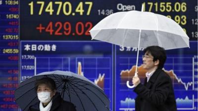 Pedestrians walk past stock market boards