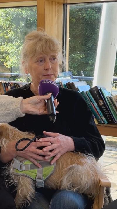 A woman with blonde hair sat down with a dog on her lap