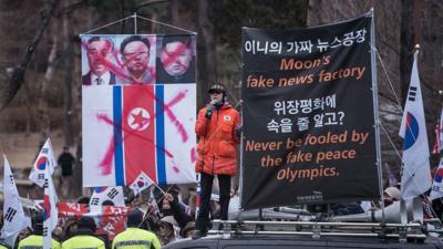 Protesters hold a sign with North Korean leaders' faces crossed out.