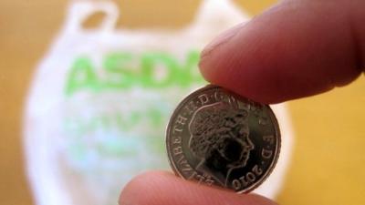 Man's fingers holding 5p with plastic bag in the background