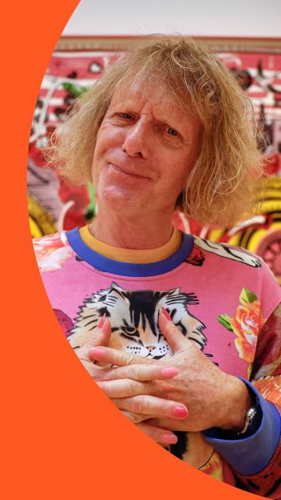Artist Grayson Perry, wearing pink patterned jumper, wearing pink nail polish and smiling to the camera.