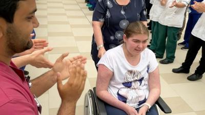 Freya in a wheelchair being clapped out of hospital