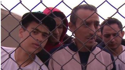 Ibrahim Maarouf (c) and other migrants behind a wire fence at military base in Dhekelia