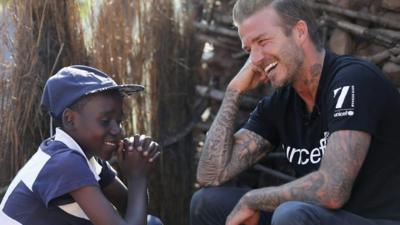 A child laughs with David Beckham