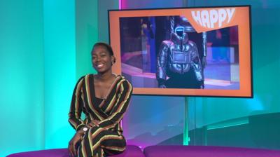 Shanequa in the studio with a robot in the screen