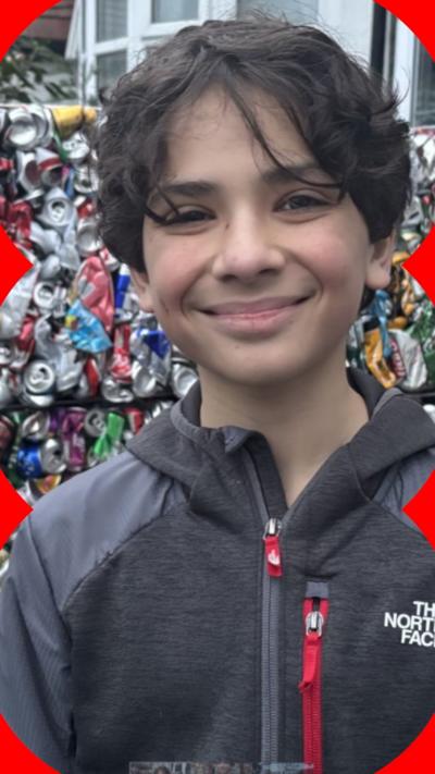 A boy with black hair and a grey coat stood in front of crushed aluminium cans
