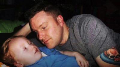 A still image of Brad Waston lovingly looking at his seriously ill son Archie