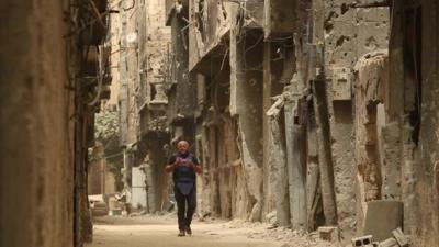 Jeremy Bowen walking down deserted, ruined street