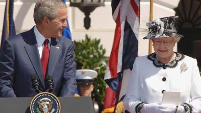 George W. Bush looks sheepishly at Queen during a speech