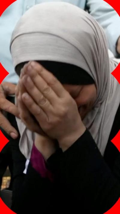 A woman in a headscarf clasps her hands in anguish.