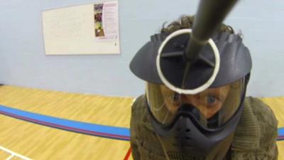 Close up of BBC reporter Mike Bushell in a helmet with a rubber-suckered archery bow stuck on his helmet