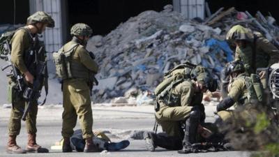 Israeli soldiers tend to their injured colleague next to the corpse of a dead Palestinian