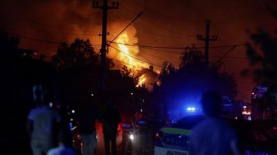 Emergency services look on as a fuel station explodes in the background.