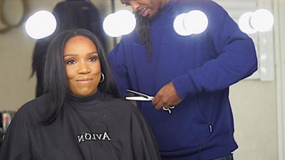 BBC presenter Roshan Roberts sits in chair while hairdresser prepares to cut her hair with scissors