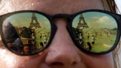 People cooling off in the Trocadero fountains across from the Eiffel Tower are reflected in sunglasses in Paris