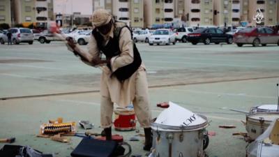 A member of Islamic State's religious police smashes up a drum-kit in the streets of Sirte with a sledgehammer, since it is deemed an un-Islamic musical instrument.