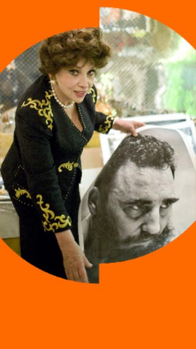 A woman with curly dark stands next to a large black and white phot of Castro's face