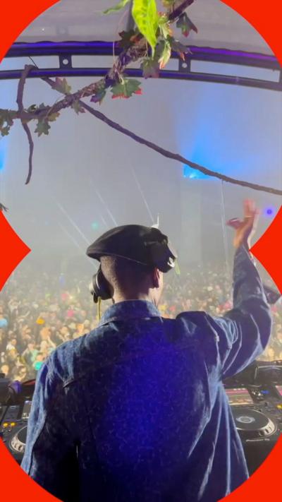 A woman wears a hat and headphones and has her arm raised in front of a crowd