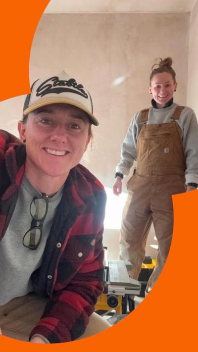 Two women, one wears dungarees, one wears a hat, using building tools