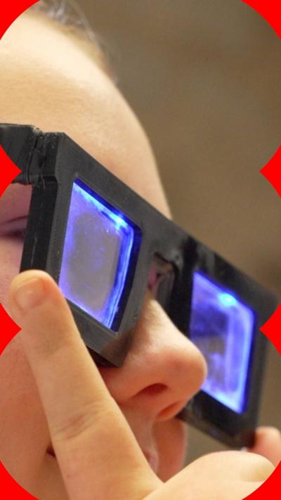 A young girl wears glasses with thick black frames, and blue light illuminating the lenses.