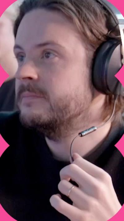 A man in a black top wears a headset and holds the mic part in his hand while he listens to someone