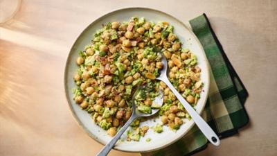 Aerial view of broccoli and chickpeas in a bowl with two spoons in it. It sits on a green checked napkin