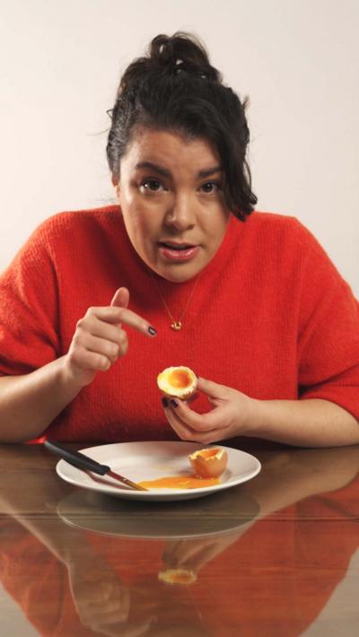 A woman wearing an orange top pointing at a boiled egg