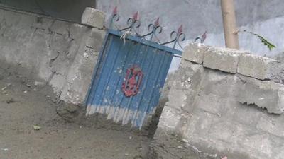 Mud from a flash flood piles up against a wall and gate to a compound