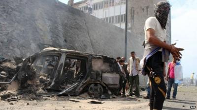 Yemenis gather around the wreckage of a car at the site of a blast that hit the convoy of the governor of Aden