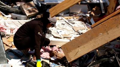 A woman searches a damaged building