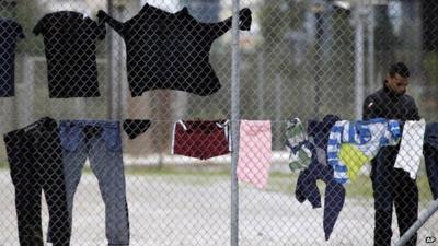 A migrant stands near clothes hanging on a fence at a former Olympic indoor stadium in southern Athens, which is being used as a temporary shelter